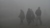 People walk through heavy smog on the outskirts of Lahore, Pakistan, on Dec. 14, 2023.