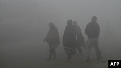 People walk through heavy smog on the outskirts of Lahore, Pakistan, on Dec. 14, 2023.
