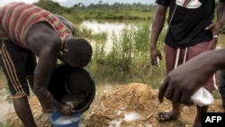 FILE - A group of illegal gold panners wash sand collected from a riverbed as they look for specks of gold, in Kibi area, southern Ghana, April 12, 2017.