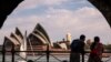 A couple watches boats as they stand on the harbor foreshore opposite the Sydney Opera House in Sydney on Oct. 1, 2023.