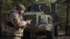 FILE - A Ukrainian soldier checks his phone while standing in front of a Swedish self-propelled Archer howitzer system at the front line in Ukraine's Donetsk region, March 4, 2024.