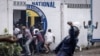 FILE - A Police officer throws a rock as opposition supporters run into a opposition leader Martin Fayulu's party house during a demonstration in Kinshasa, Democratic Republic of Congo, Dec. 27, 2023.