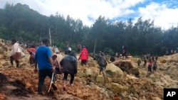 In this photo provided by the International Organization for Migration, people cross over the landslide area to get to the other side in Yambali village, Papua New Guinea, May 24, 2024.