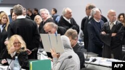 A defendant hides her face behind a folder in the courtroom, as defendant Prince Heinrich XIII Reuss (top, 2ndR) stands next to his lawyers in a courtroom in Frankfurt am Main, May 21, 2024.