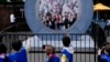 Children signal to pedestrians in Dublin, Ireland, through a livestream portal as part of an art installation on the street in New York, May 14, 2024.