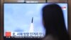 A woman walks past a television showing a news broadcast with file footage of a North Korean missile test, at a railway station in Seoul on March 9, 2023.