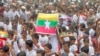 Rohingya refugees gather in the rain, with a flag of Myanmar seen at center, to demand safe return to Myanmar's Rakhine state as they mark the seventh anniversary of their exodus at their refugee camp in Cox's Bazar district, Bangladesh, Aug. 25, 2024. 