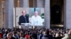 Monsignor Paolo Braida reads next to Pope Francis as they appear on a screen in St. Peter's Square, during the Angelus prayer led by Pope Francis from Santa Marta chapel at the Vatican, Nov. 26, 2023. 