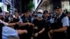 A member of the public is escorted by police after light a smartphone light near Victoria Park, on the 34th anniversary of China's Tiananmen Square crackdown in Hong Kong, June 4 2023. 