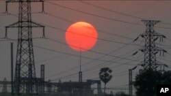 FILE - The sun sets behind electricity pylons in Krang Tnung village on the outskirts of Phnom Penh, Cambodia, Dec. 26, 2019.