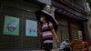 A man wearing a face mask and holding an umbrella to shield himself from the sun walks by an elderly man collecting recycle items in front of vacant shop lots at Qianmen Street in Beijing, Aug. 17, 2022.