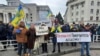 Люди тримають українські прапори та транспаранти з написом «Ми – українці», по центру та «Окупанти! Повертайтеся додому!». під час мітингу проти російської окупації на площі Свободи в Херсоні, Україна, субота, 5 березня 2022 р. (AP Photo/Олександр Чорний)