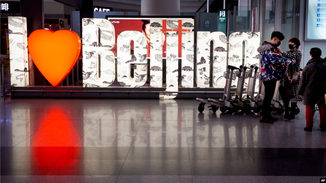 Los viajeros que llevan máscaras faciales se abrazan cerca de un letrero que dice "Amo Beijing" en el Aeropuerto Internacional Capital de Beijing.
