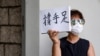 A woman holds up a paper pad that reads "support sibling" while waiting outside the court to bid farewell to a prison van transporting Tong Ying-kit in Hong Kong