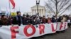 People hold a banner as they walk in front of the Supreme Court building