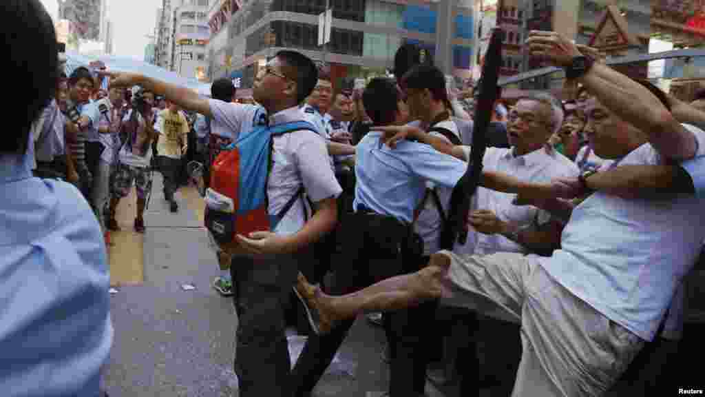 A pro-democracy protester, left, argues with an anti-Occupy Central protester, not shown, while being kicked by another anti-Occupy Central protester, right, at Hong Kong's shopping Mongkok district, where a main road is occupied, Oct. 3, 2014. 