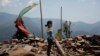 In this April 8, 2016 photo, Khendo Tamang, 8, stands near the debris of the collapsed home she was trapped in after the April 25, 2015 earthquake struck in Banskharka, Nepal.