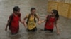 FILE - Indian girls hold hands and wade through a waterlogged street .