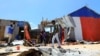Des civils marchent près de la scène où un tir de mortier a détruit des maisons à l'extérieur d'un complexe tentaculaire qui abrite la base de la Mission de l'Union africaine en Somalie (AMISOM) à l'aéroport de Mogadiscio, en Somalie, le 25 mars 2021.