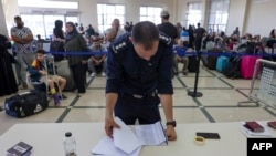 A Palestinian border guard checks the documents of dual nationals and foreigners as they wait to cross the Rafah border crossing with Egypt, in the southern Gaza Strip, Nov. 7, 2023.