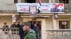 FILE - A Syrian police officer walks past a group of local people standing at a building with a portrait of Syrian President Bashar al-Assad in Salma, Syria, Jan. 22, 2016. 