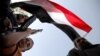 A boy holding a weapon stands under a Yemeni national flag, as followers of the Houthi group demonstrate against an arms embargo imposed by the U.N. Security Council on the group in Sanaa, April 16, 2015.