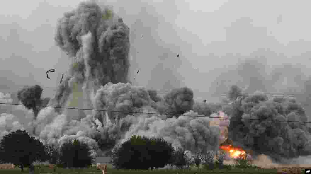 Une épaisse fumée, des débris et des flammes s’élèvent après une frappe aérienne de la coalition menée par les Etats-Unis à Kobani, en Syrie alors que des combats s’intensifient entre les Kurdes Syriens et des combattants de l’Etat Islamique, comme observé depuis les faubourgs de Suruc, à la frontière Turco-Syrienne, dimanche le 12 octobre 2014. (AP Photo/Lefteris Pitarakis)