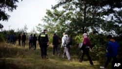 Seorang polisi federal Jerman mengawal satu kelompok migran yang masuk perbatasan Jerman secara ilegal dari Polandia, di dekat Frost, tenggara Berlin, Jerman, 11 Oktober 2023. (Foto: Markus Schreiber/AP Photo)