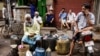 Ethnic Chinese Indians rest behind vendors selling their ware at a roadside market in Kolkata, India, Friday, June 19, 2020. India's prime minister is meeting top opposition leaders Friday as the government tries to lower tensions with China after…