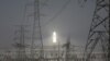 FILE - A molten salt solar tower stands behind electricity pylons at a power station near Dunhuang, Gansu province, China, April 13, 2021.