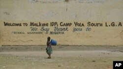 Un niño pasa frente a un cartel que da la bienvenida a refugiados que huyen de la milicia extremista Boko Haram, en Nigeria.