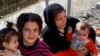 Migrant women cradle children near a fence in a makeshift encampment at Greece’s northern border town of Idomeni, March 4, 2016. (J. Dettmer for VOA)