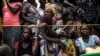 FILE - A woman looks on while people wait for their ration of food to be handed out at a food distribution Oct. 25, 2017 in Kasala, in the restive province of Kasai, Democratic Republic of Congo.
