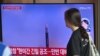 A woman walks past a television screen showing a news broadcast with file footage of a North Korean missile test, at a railway station in Seoul on July 12, 2023.