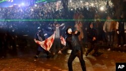 Un manifestant masqué lance un objet en direction de la police lors d'un rassemblement devant le parlement à Tbilissi, en Géorgie, 1er décembre 2024. AP / Zurab Tsertsvadze