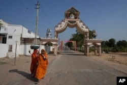Women walks past an entrance gate of Dingucha village in Gandhinagar, India, Nov. 12, 2024.