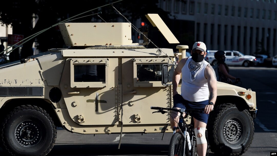 Un hombre en bicicleta pasa frente a un vehículo blindado de la Guardia Nacional cerca de la Casa Blanca, el lunes 1 de junio de 2020, cuando manifestantes se reúnen para protestar la muerte del afroestadounidense George Floyd en custodia policial.