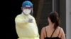 A medic wearing personal protective equipment (PPE) gestures to a woman waiting to take a Covid-19 coronavirus test at the National Olympic Stadium in Phnom Penh on February 23, 2021. (Photo by TANG CHHIN Sothy / AFP)