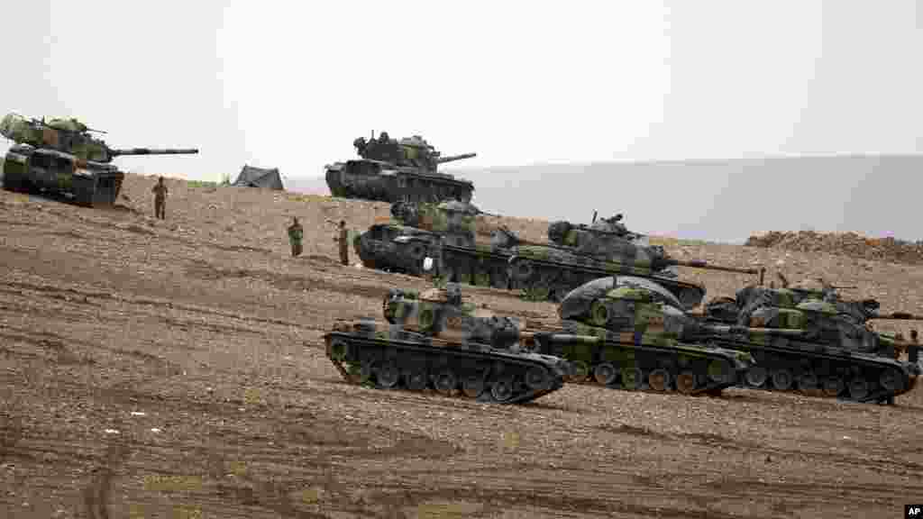 Des soldats turques tiennent leur position avec des chars d’assaut au sommet d’une colline dans le faubourg de Suruc, à la frontière Turco-Syrienne, observant Kobani, en Syrie, au cours des combats entre les Kurdes Syriens et les combattants de l’Etat Islamique, dimanche le 12 octobre 2014. (AP Photo/Lefteris Pitarakis)