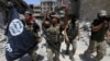 FILE - Members of Iraq's Emergency Response Division hold an Islamic State flag that they pulled down as they celebrate in the Old City of Mosul, Iraq, July 8, 2017. Islamic State fighters have mostly been pushed out of Iraq and Syria but are far from defeated.