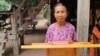 Im Chaem stands behind a podium holding her Bible in front of her home in O'Angre village, Anlong Veng district, Oddar Meanchey province, Cambodia. (Courtesy photo of Pastor Touch Chanthou)