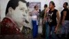 Personas buscan sus nombres en el padrón electoral cerca de un mural dedicado a Hugo Chávez, el domingo, durante las elecciones municipales en Caracas.