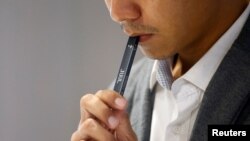 FILE PHOTO: A shopkeeper demonstrates smoking a Juul brand vaping pen to customers at a Juul shop in Jakarta