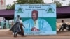 Des femmes passent devant une affiche de campagne de l'ancien président du Niger et candidat à la présidence, Mahamane Ousmane, le 18 février 2021 à Niamey.