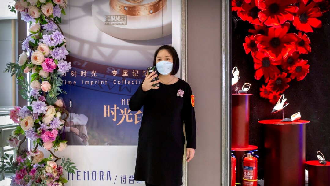 Un empleado usa una máscara facial mientras está parada afuera de una tienda en un centro comercial en su mayoría vacío en Beijing, el sábado 7 de marzo de 2020.