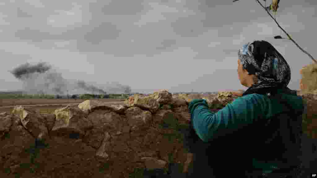 Une Kurde Turque, débout à Muritpinar, dans les périphéries de Suruc, à la frontière Turco-Syrienne, contemple la fumée venant des flammes causées par les frappes au cours des combats entre les combattants de l’Etat islamique et les forces kurdes, en Syrie, dimanche le 12 octbre 2014. (AP Photo/Lefteris Pitarakis)