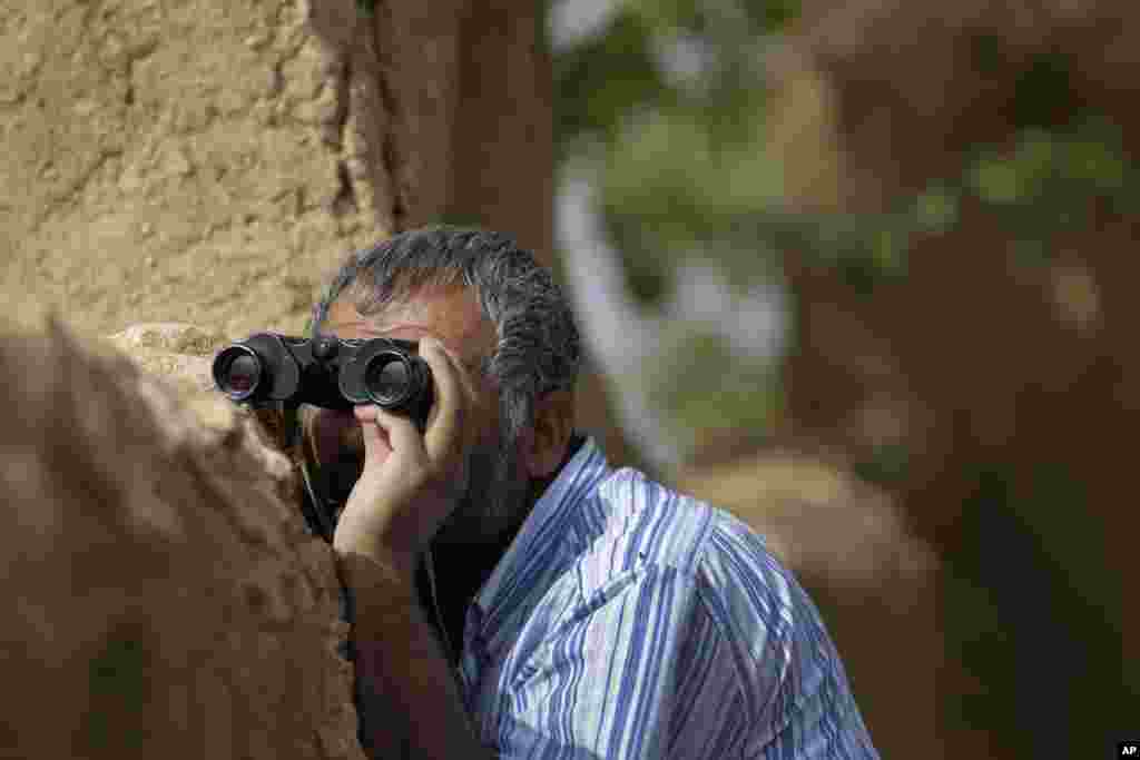 Un Turc Kurde regarde à travers des jumelles à Mursitpinar, dans les périphéries de Suruc, à la frontière Turco-Syrienne alors que des combats font rage entre les combattants de l’Etat islamique et les forces kurdes à Kobani, en Syrie, le 12 octobre 2014. (AP Photo/Lefteris Pitarakis)