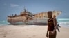 A masked Somali pirate stands near a Taiwanese fishing vessel that washed up on shore after the pirates were paid a ransom and released the crew, in the once-bustling pirate den of Hobyo, Somalia, Sept. 23, 2012. 