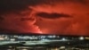 Houses in the village of Hafnarfjordur are seen as smoke billows in the distance and lava colors the night sky orange from a volcanic eruption on the Reykjanes peninsula, western Iceland on Dec. 18, 2023.