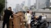 A woman wearing a mask walks past delivery workers moving boxes in Beijing on Aug. 20, 2020. U.S. and Chinese trade envoys discussed strengthening coordination of their government’s economic policies during a phone meeting Tuesday, Aug. 25, 2020,…